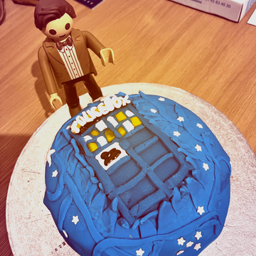 Un gâteau d'anniversaire écrit avec un tardis (en pate à sucre) qui en sort et grand Playmobil Doctor Who à côté